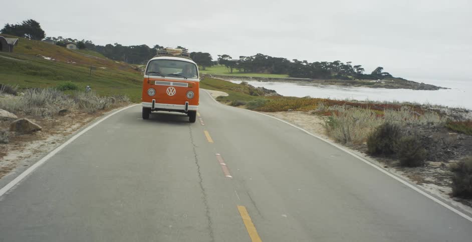 A volkswagen bus drives on a coastal road