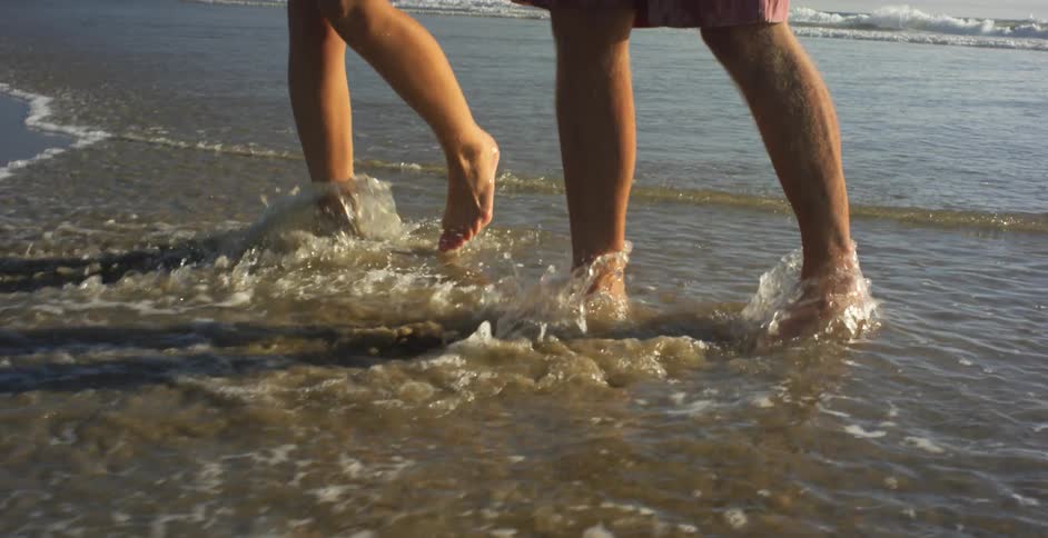 A man and woman walk on the beach as the tide flows in