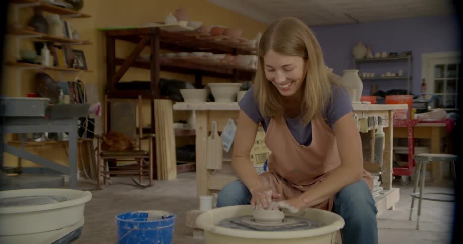 A woman in a pink apron smiles as she makes pottery