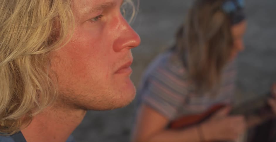 A man eats and nods his head as a woman plays guitar