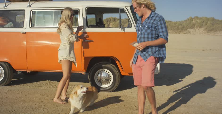 A man and woman walk onto a beach with their dog