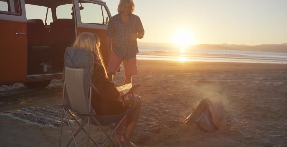 Two people sit by the campfire on the beach