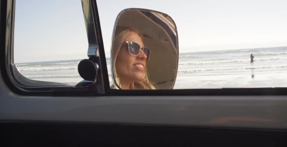 A woman smiles while riding in a car on the beach