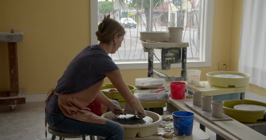 A woman is forming clay on a wheel