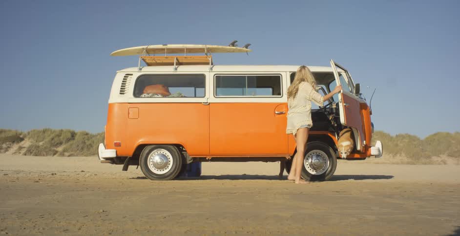 A couple and dog climb out of a volkswagen van on a beach