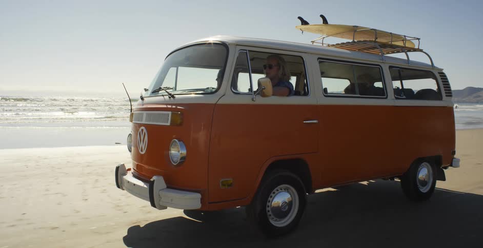 A man drives a volkswagen bus on a beach