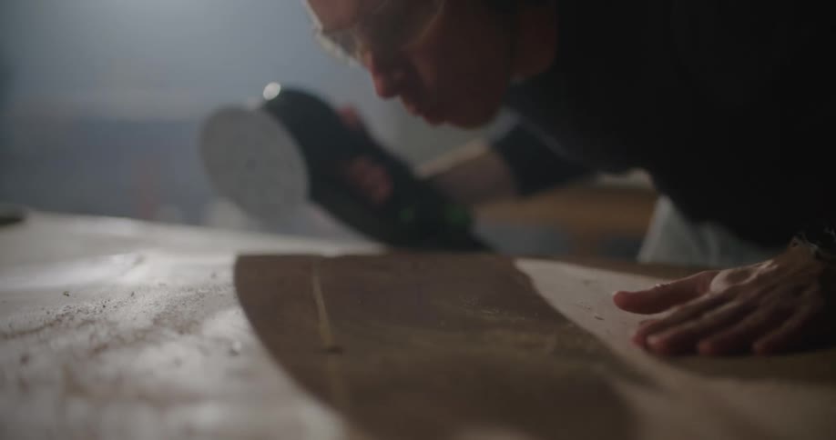 A man uses a power sander to finish and smooth the surface of a wooden table