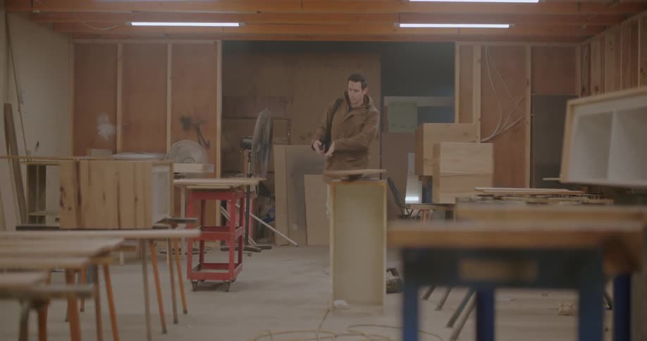 Young man wearing a brown jacket turns on the lights on a carpentry workshop