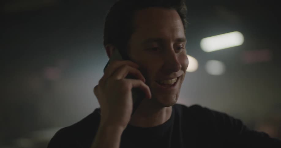 A man laughs while talking on his phone inside a dimly lit business