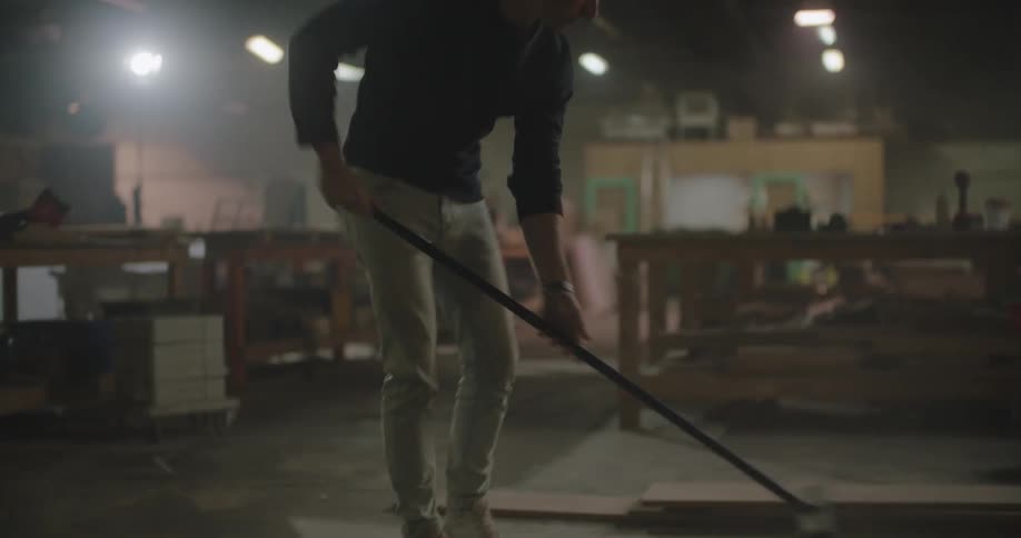 Man sweeps floor near work benches kicking up dust