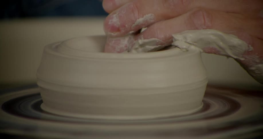 A hand molds clay on a pottery wheel