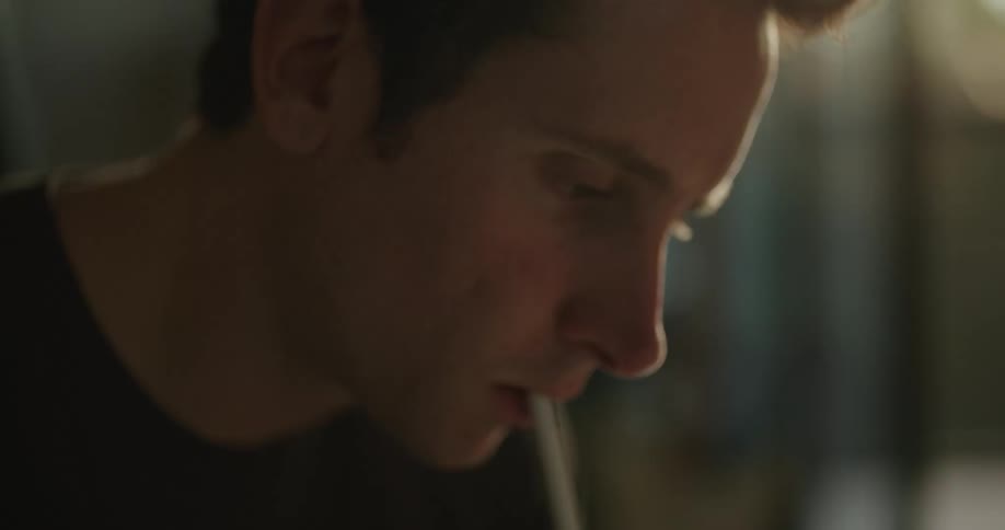 A man tabs a stylus against his face while lost in thought before drawing on a tablet while sitting indoors during the day