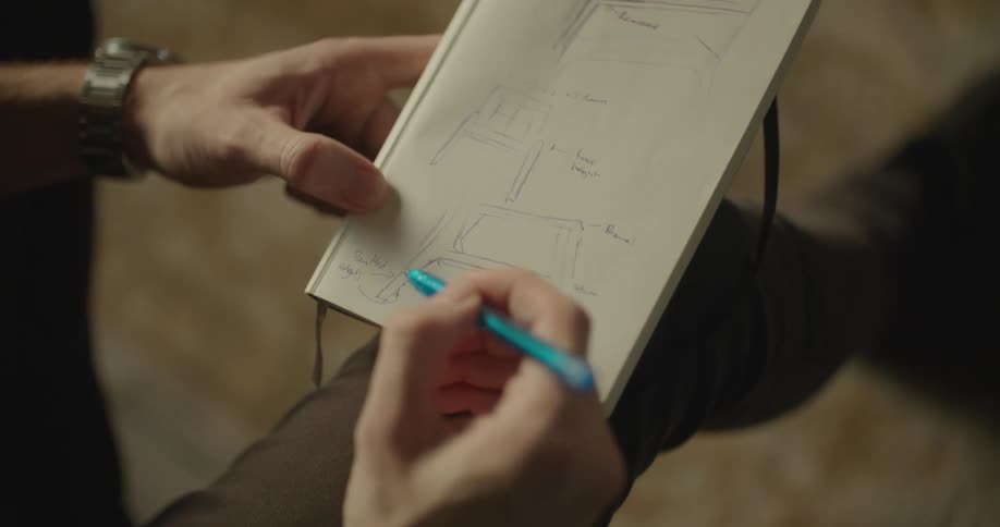 Man sits sketching with pencil on drawing pad
