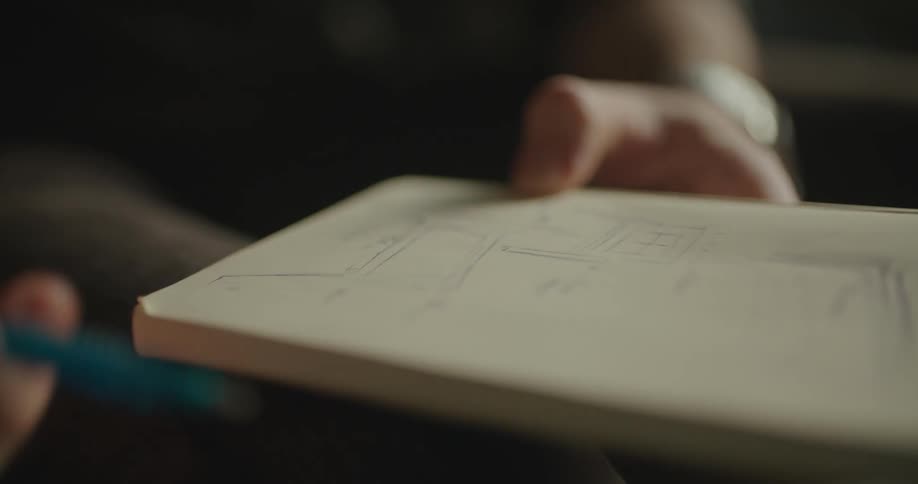 A man makes a sketch of furniture using a pen in his notebook