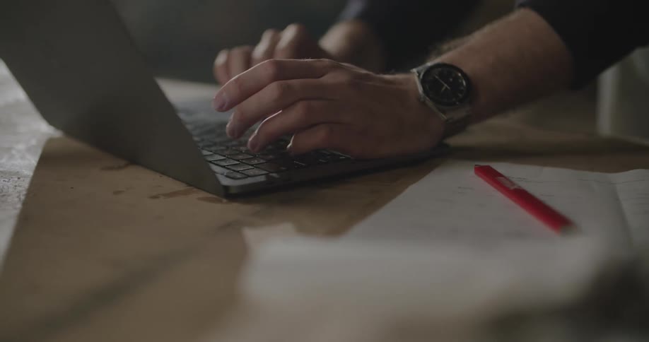 A man typing on a laptop and writing on paper