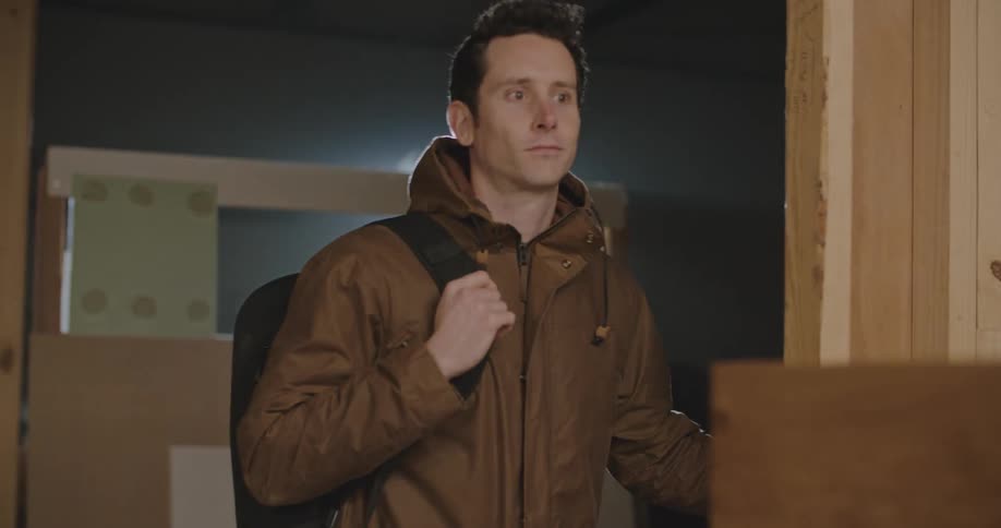 A man throws his backpack over his shoulder and smiles while turning off the lights to a woodshop