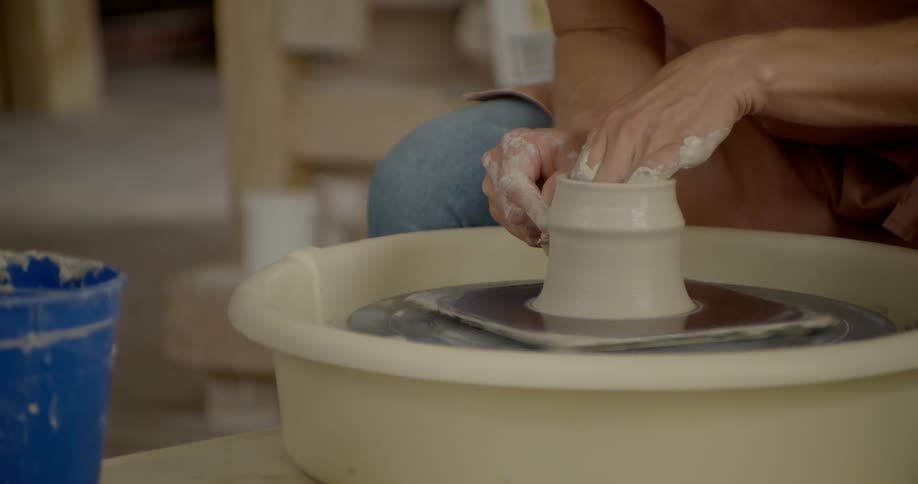 A person spins clay into a shape using a pottery spinning wheel