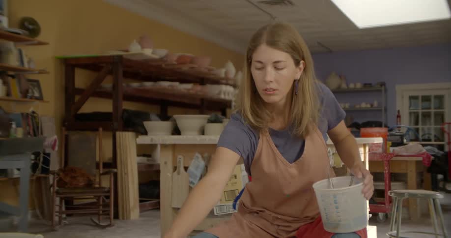 A woman in a pink apron pulls string from a bucket