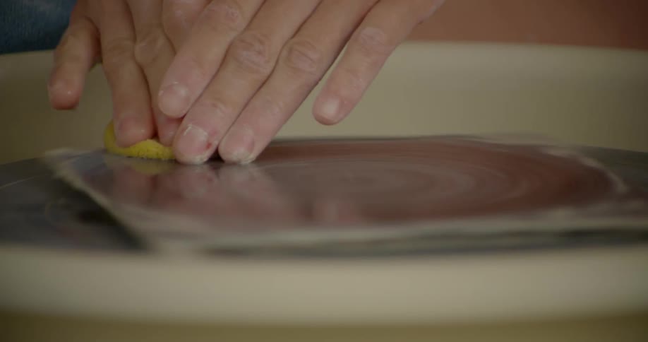 A man spins and wipes a spinning pottery wheel