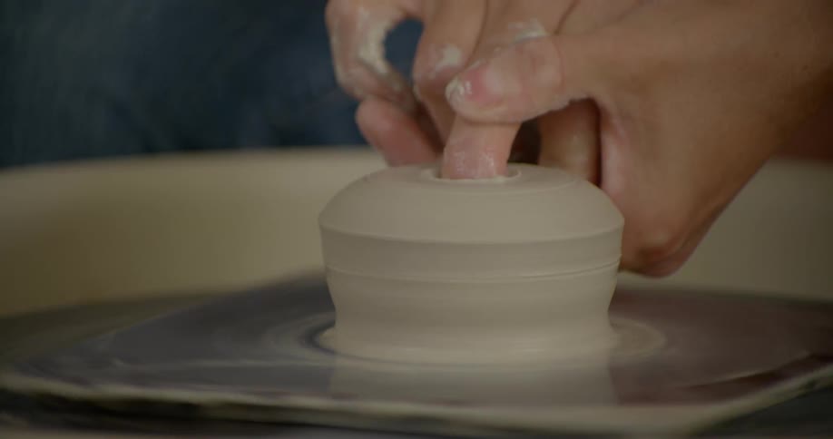 Hands mold clay on a pottery wheel