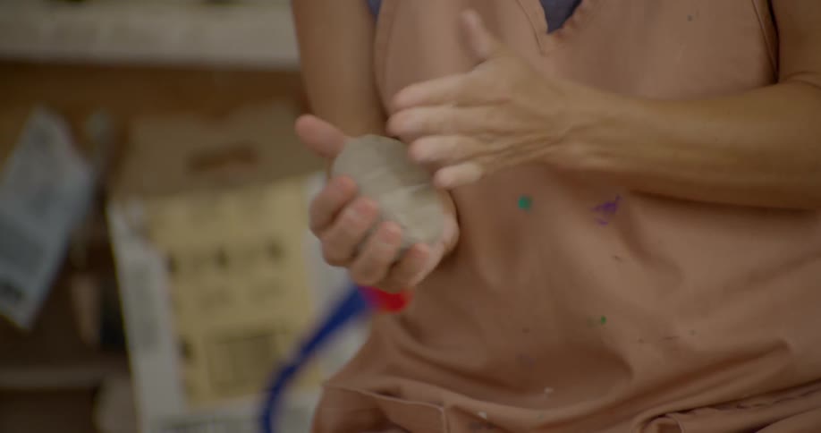 A woman pounds some clay in her hands