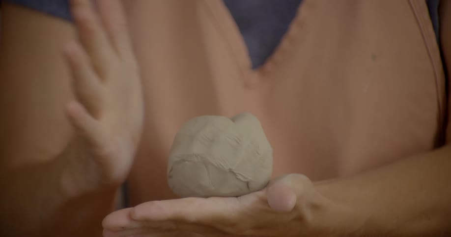 A person pats a ball of clay in between their hands