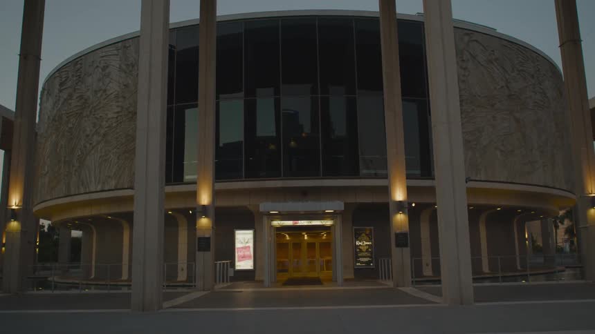 A circular building with a large shaded window under a cloudy sky in the evening