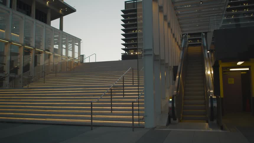 An empty wide staircase next to an up escalator in a city at dusk