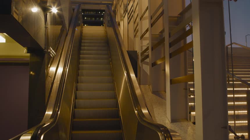 A working escalator going downward is unused in a commercial building at dusk