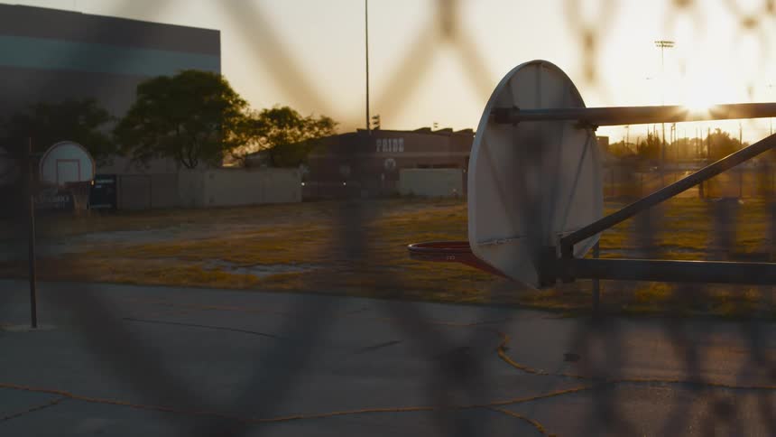 The sun sets over a basketball court in a park outside of a building