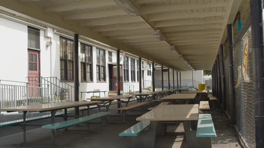 Picnic tables sit in rows between fence and buildings