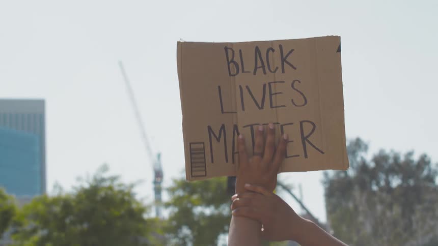 A protester holds a black lives matter sign into the air while standing outdoors during the day