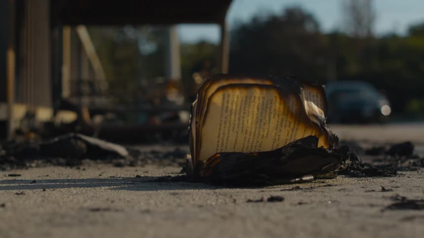 A book with burnt pages with a road vehicles trees the sky and clouds in the background