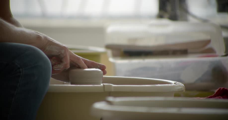 An artisan works a clay form on a pottery wheel with his hands and water