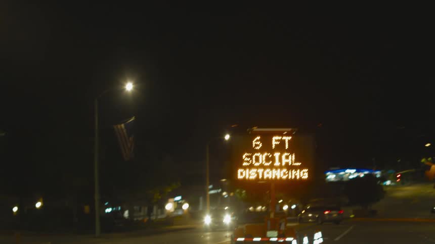 A powered traffic sign advocating wearing a mask and social distancing in a road at night