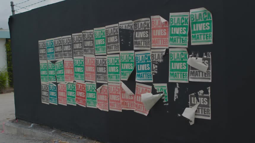 Old black lives matter posters posted in rows on a wall outdoors during the day