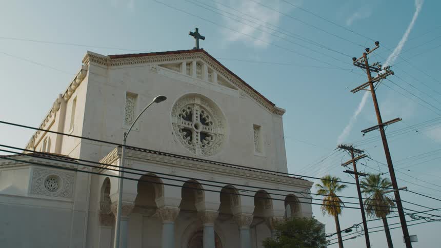 Electric poles and cables in front of a small church under a blue sky at morning