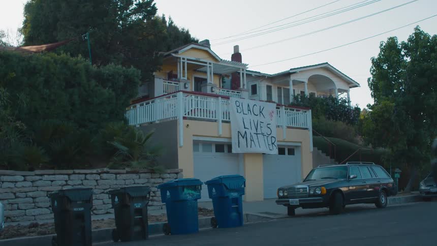 Station wagon sits parked in front of a building that has a sign hanging from a balcony railing