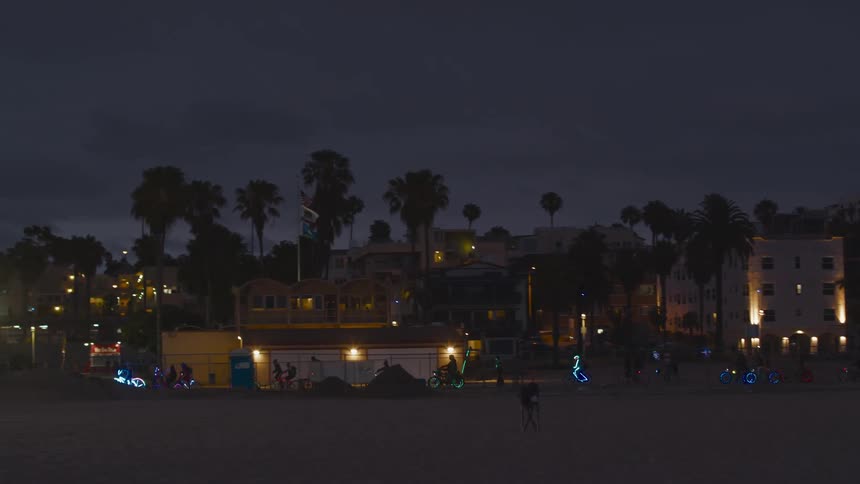 A group of people ride past a park on bicycles with neon lights in the spokes