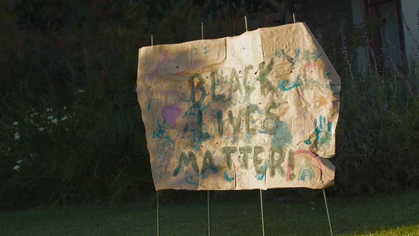 A tattered and hand painted black lives matter sign sits in a neighborhood