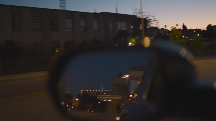 The side view mirror of a car as it travels through a city at sunset