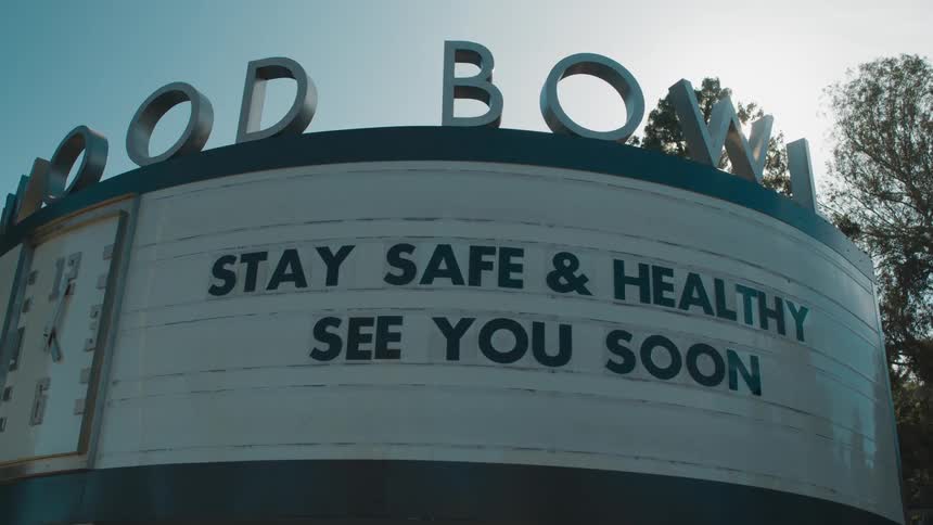 A curved business sign with a clock outdoors during the day
