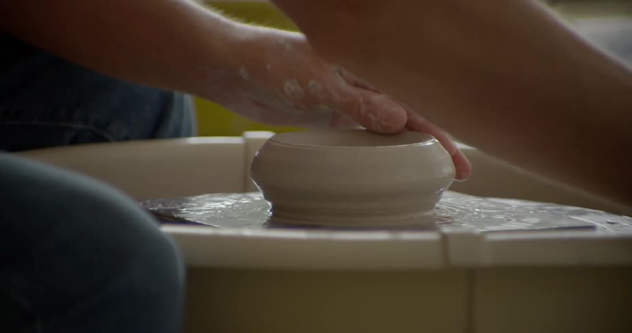 Hands mold clay on a pottery wheel