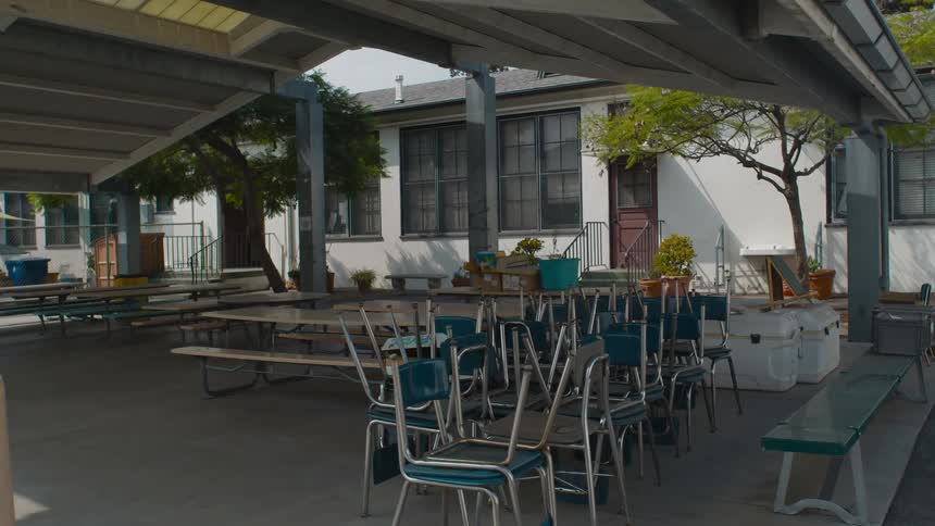 A cafeteria with chairs benches and tables with a building and trees in the background