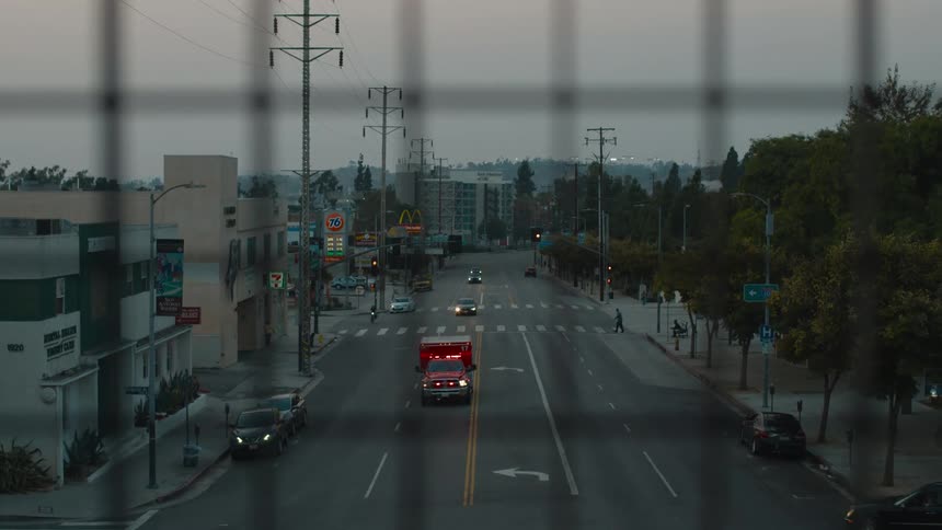 An ambulance with lights flashing turns a corner and travels down a street and under an overpass