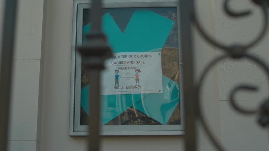 Sign on a billboard at the side of a church behind an iron fence