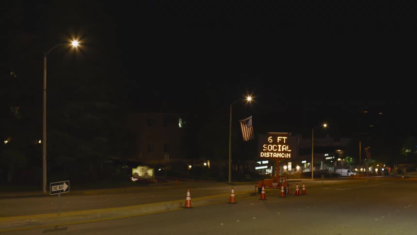 Road sign presenting covid19 social distancing message blinks by empty road at night