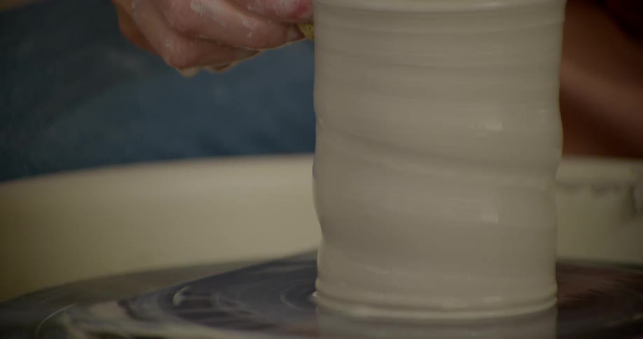 A person making designs in a clay cup