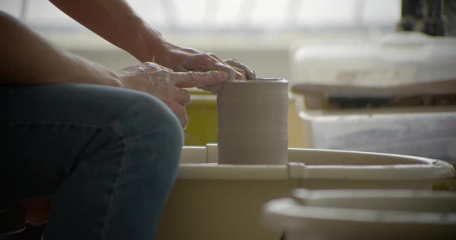 An artist works a clay form on a pottery wheel