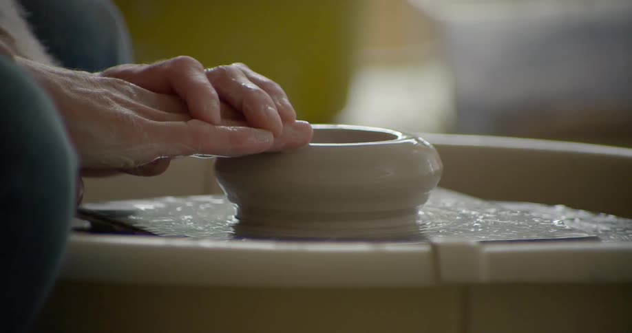 Two hands form clay on a wheel